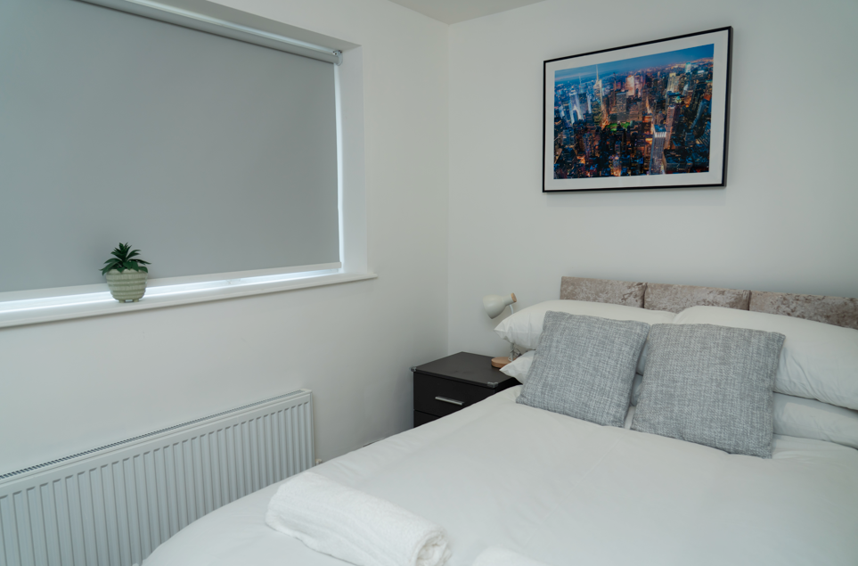 Clean modern bedroom with double bed, city skyline artwork, and minimalist hotel-style décor