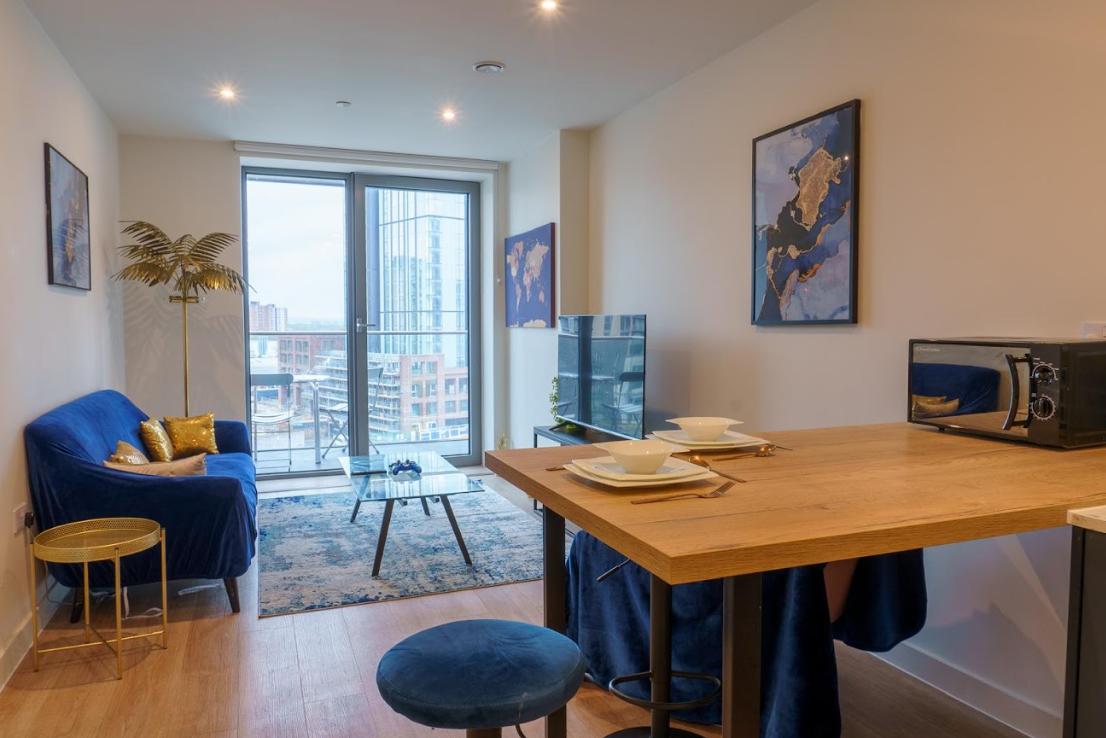 Modern city apartment with floor-to-ceiling windows, blue velvet sofa with yellow cushions, wooden dining table, and stunning city skyline views