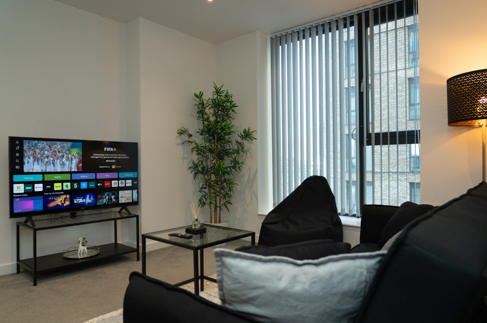 Modern loft living area with dark sofa, glass coffee table, large windows with city views, and entertainment system